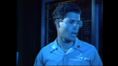 1980s: Officer in Navy control room talks, points to map on wall. Officer continues talking to men in room. Man in room talks. Airplane on airfield.