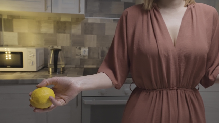 Close up of a slim woman in a brown home dress throwing fresh lemon from one hand to another. Action. Concept of cooking food at the kitchen at home.