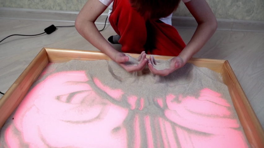 The child draws on the light table with his hands. Drawings in the sand. Art therapy. Fingers draw in the sand. The development of imagination. Patterns. The table is illuminated. Heart.