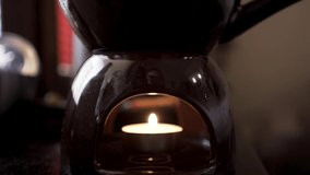 Close up of a small burning candle inside a candlestick with aroma oil. Action. Concept of meditation and relaxation in a calm dark atmosphere. 
