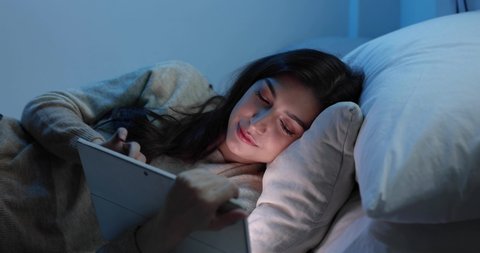 Woman are using the tablet computer on the bed before she sleeping at night, Mobile addict concept, Blue light harmful to the eyes.