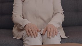 The old woman, sitting on the sofa, with her hands on her knees, puts her hands together.  United hands, lifed and aged hand portrait. Slow motion video.Close up.