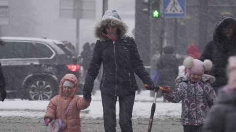 Kiev, Ukraine, March 2021: Woman with children cross the road at a crossroads in the city during a snowfall on a winter evening. Close-up. Traffic on the street of the city