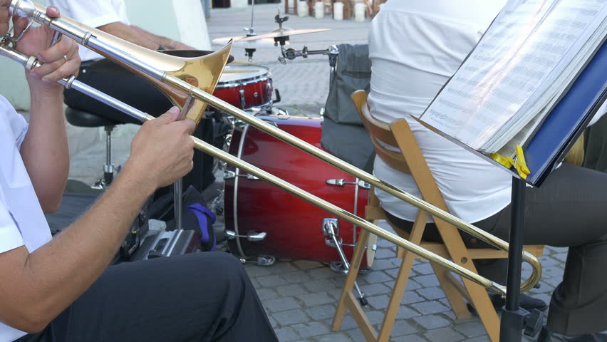 Man is playing on trombone along with orchestra. The trombone is a musical instrument in the brass family.