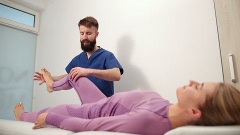 Therapist doing healing treatment on female leg, knee. Chiropractic, osteopathy, manual therapy. Alternative medicine, pain relief concept. Physiotherapist work with foot. Bearded man in hospital