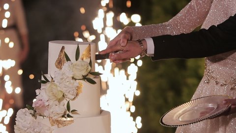 Cut the wedding cake. The bride and groom cut the wedding cake. Wedding cake with sparklers in several tiers. Detail of wedding cake cutting by newlyweds