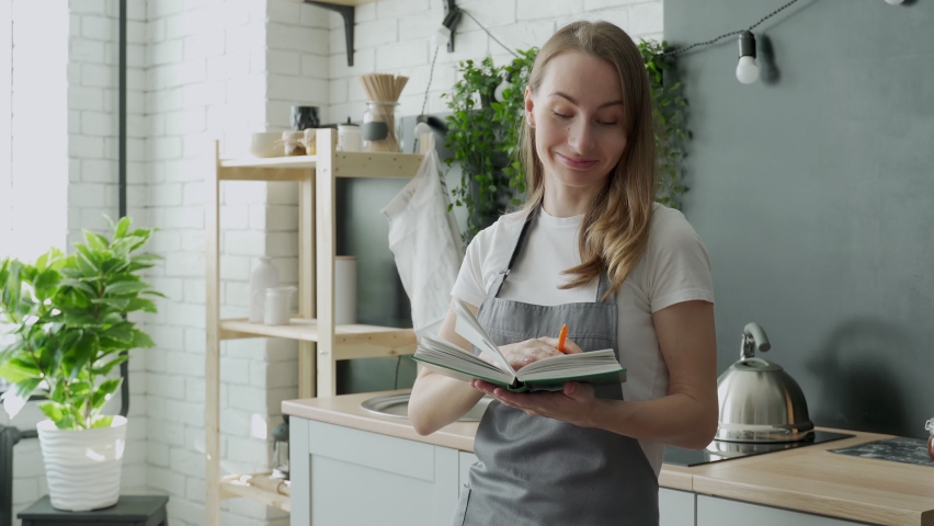 Young woman reading cookbook in the kitchen, looking for recipe Royalty-Free Stock Footage #1069328770