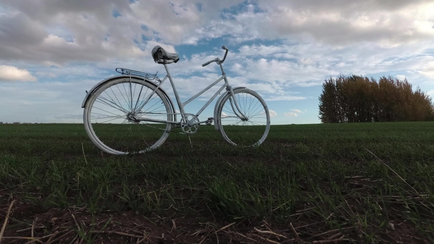 Old white bicycle on field and clouds motions, time lapse