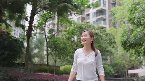 4k slow motion of happy Young Chinese woman walking happily in her neighborhood The new urban residential building is behind Real estate concept video
