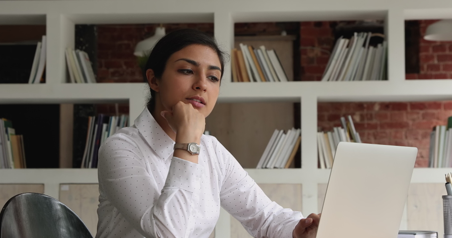In modern office thoughtful brooding young Indian ethnicity woman work on laptop do remote freelance job look pensive, ponder new idea. Student sit in library makes coursework thinks over task concept Royalty-Free Stock Footage #1069342522