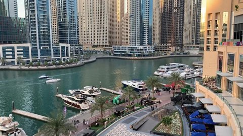 Dubai  UAE - September 26, 2020: Beautiful view of Dubai Marina promenade and river from Marina Mall with many people before the sunset. Beautiful view of Marina walk with green nature, yachts, cafes.