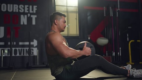 Asian professional Athlete or Sportsman trainer working out his abdominal muscles by holding the medicine ball exercise twist left and right sitting in the modern loft gym. Health and fitness concept.