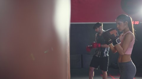 Asian professional male and female athlete people wearing sports clothes and boxing gloves, doing workout exercise by hitting a punching bag or Boxing Sandbag to maintain muscle in gym or fitness club