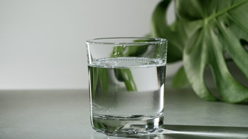 Chlorophyll extract is poured in pure water in glass against a white grey background with green leaf. Liquid chlorophyll in a glass of water. Concept of superfood, healthy eating, detox and diet Royalty-Free Stock Footage #1069349443
