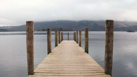 Slowly walking a long wooden jetty with poles to reveal view of Derwentwater in the Lake District.