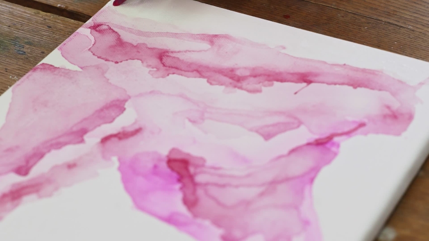 Close up of female artist paints an abstract picture, he pours a pink paint fron tube on wet canves