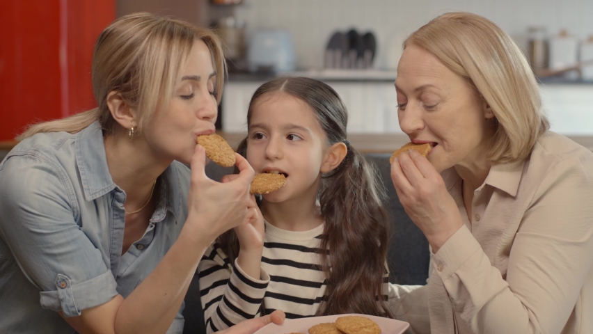 Three generation woman happy family old grandmother, teenage daughter and kid girl are eating cookies. Loving child grandson laughing at mother grandmother at home. | Shutterstock HD Video #1069359664