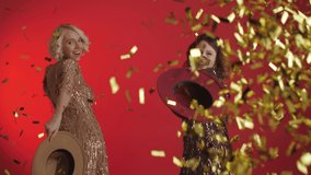 Joyful women wearing sequin dresses are dancing at the party. Out Of Hat falling confetti. Celebrating New year, Christmas, birthday concept. Isolated on red background. - Powered by Shutterstock - Get 15% off with code: PIKWIZARD15
