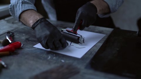 Linocut concept. Rolling to make a pressure on a piece of linoleum in a form of a bird. Male in black gloves rolling on cut stamp to make a print on paper. 4k footage