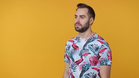 Joyful cheerful shocked bearded young man 20s in summer t-shirt isolated on yellow color background studio. People lifestyle concept. Screaming on megaphone pointing index finger aside clenching fists