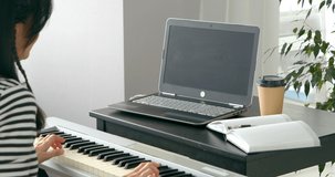 Close-up shot of unrecognizable woman playing electronic piano while learning music online using laptop at home 
