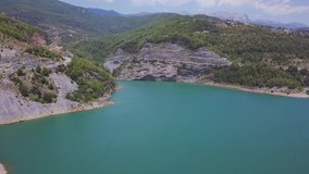 Aerial view of amazing blue lake surrounded by rocks. Clip. Beautiful turquoise water of a big lake and forested mountains.