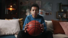 Serious black man teenager holding basketball ball and sitting in living room, young teen athlete, sport portrait at home, kid preparing for watching professional game on tv. - Powered by Shutterstock - Get 15% off with code: PIKWIZARD15