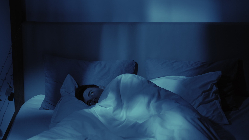 Night insomnia. Sleep disorder. Depression anxiety. Disturbed thoughtful guy awake late lying in bed alone at home in dark blue light. Royalty-Free Stock Footage #1069375492