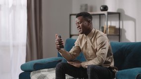 happy black guy is chatting by video call with friends and smiling looking at camera of smartphone, sitting alone at home, video chat in social nets, distant communication