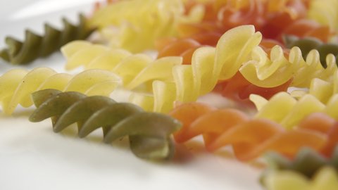 Raw colored spiral pasta in a white plate. Close-up. Dolly shot. Macro