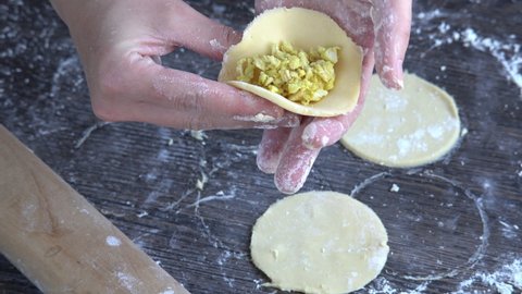 Pelmeni dumplings making process: Woman's hand shaping raw pelmeni dough stuffed with chicken filling. Gluten free recipe for traditional Russian cuisine. Floured wooden surface, handmade dumplings.