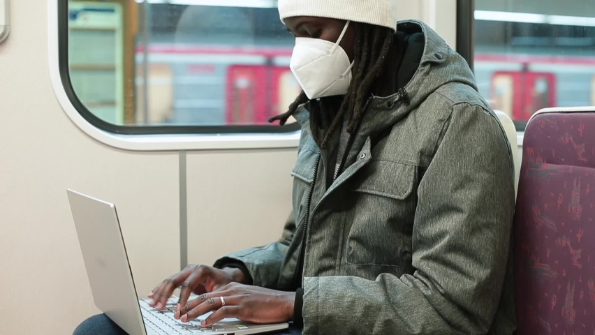 Hands pushing buttons, doing urgent work. Waiting train depart train. Afro man in mask uses wifi laptop passenger seat on train. Freelancer life at lockdown. Respect face mask COVID-19.  Royalty-Free Stock Footage #1069390543