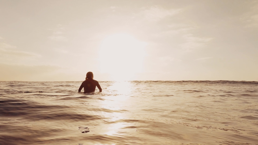 One surfer man surfing and sitting on his surfboard in the sea or ocean at the beach outdoor. Underwater view of wave crashing barrel.
