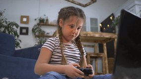 Happy girl playing video games with a joystick. Child gambling addiction. Happy little girl playing video game home. Concept of child gambling addiction. Happy little girl learning to work on laptop