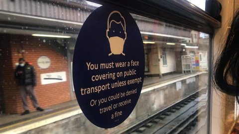 Blue circle Covid Mask wearing sign sticked on a window seeing platform of a running London overground tube in central London with. Covid measure on public transport. London 21 DEC 2020.