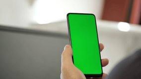 Handheld Camera: Point of View of Man at Modern Room Sitting on a Chair Using Phone With Green Mock-up Screen Chroma Key Surfing Internet Watching Content Videos Blogs Tapping on Center Screen