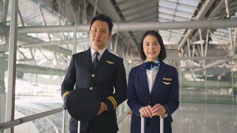 Portrait of attractive Asian airliner pilot and air hostess standing in airport terminal smiling with confidence and happiness. Commercial airplane cabin crew or hostess and pilot occupation concepts.
