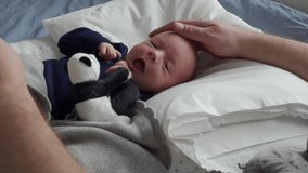 father playing with newborn baby, baby boy lying in baby pod nest, father's hand holds a soft toy.