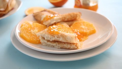 Thin pancakes crepes. Woman hand pouring on the crepes orange sweet sauce marmalade.
