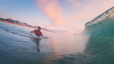 Surfer and wave. Happy male surfer shows the shaka sign before getting barrelled by the wave. Surfer passes first barreling wave and then dives under the second wave