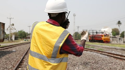 Portrait of handsome Africa American engineering using walkie talkie for control labor with laptop in front of train garage. Back view of contractor on background of outdoor old train garage.
