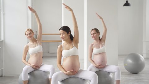 Young pretty pregnant woman in sportive outfit stretching body in studio, performing sport exercise while preparing for childbirth. Healthy lifestyle concept.: film stockowy