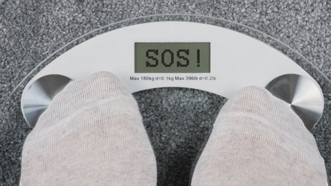 Overweight on bathroom scales.  Person steps on scales to check her weight. POV view. Inscription SOS on bathroom scales digital display