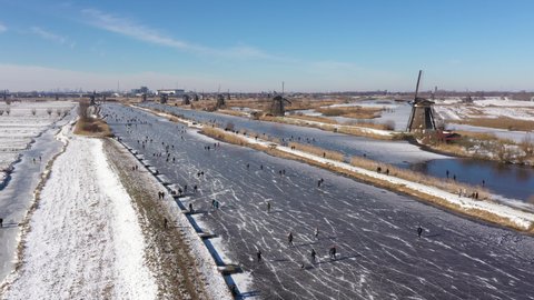 Aerial view of beautiful Winter landscape with frozen canals and snowy meadows, people ice skate past historic windmills in the Netherlands.