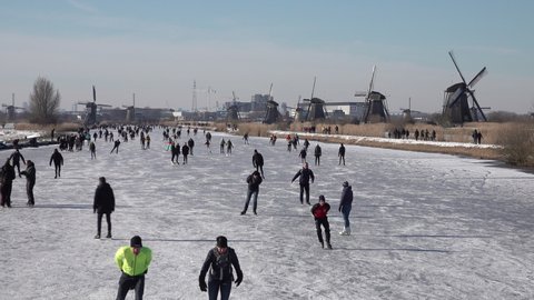 KINDERDIJK, NETHERLANDS – 13 FEBRUARY 2021: Crowds of people ice skate on frozen canals in typical Dutch town Kinderdijk, beautiful Winter scene in the Netherlands.