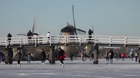 KINDERDIJK, NETHERLANDS – 13 FEBRUARY 2021: Beautiful Winter scene as people are ice skating on frozen canals in Kinderdijk town. Tradition, culture, and leisure activities in the Netherlands. 