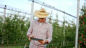 Charismatic and smiling farmer man using digital tablet in the middle of orchard to analyzing the variety of fruits concept of farming business