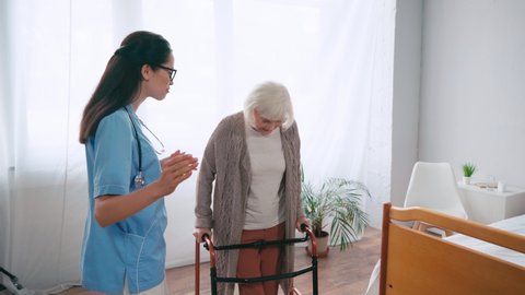 doctor pointing with hand and talking to woman stepping with walkers Video Stok