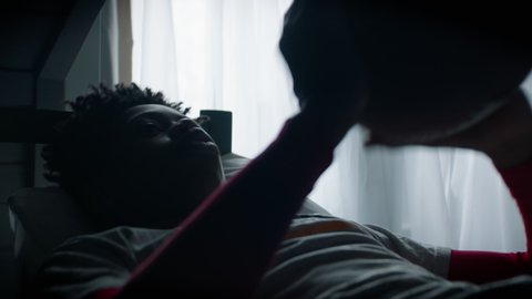 CU Silhouette of bored African American Black kid teenager boy playing with football ball in his attic bedroom at home. Shot with 2x anamorphic lens