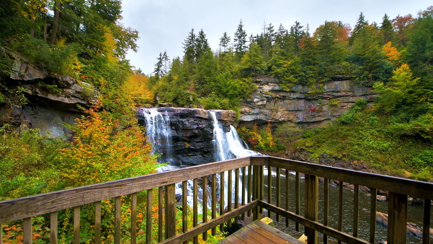 Point of view pov walking handheld shot of Blackwater Falls waterfall wooden boardwalk railing in state park, West Virginia at colorful autumn fall season with water flowing
